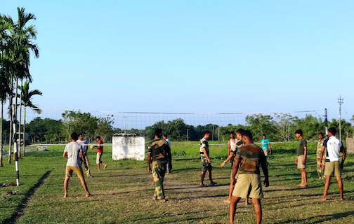 A group of men, some in camouflage, play volleyball at an outdoor net.
