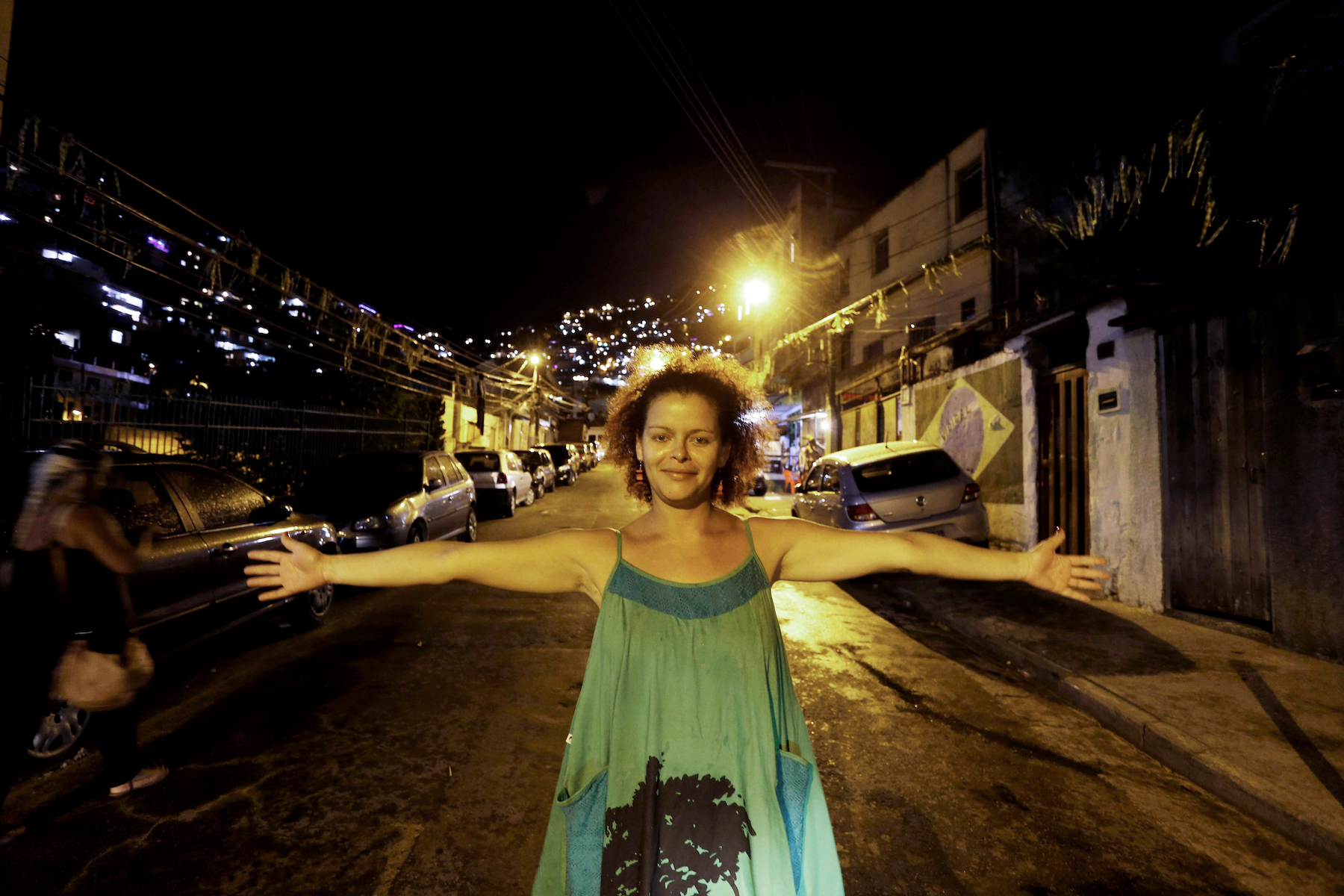A woman poses with her arms outstretched in a neighborhood street at night.