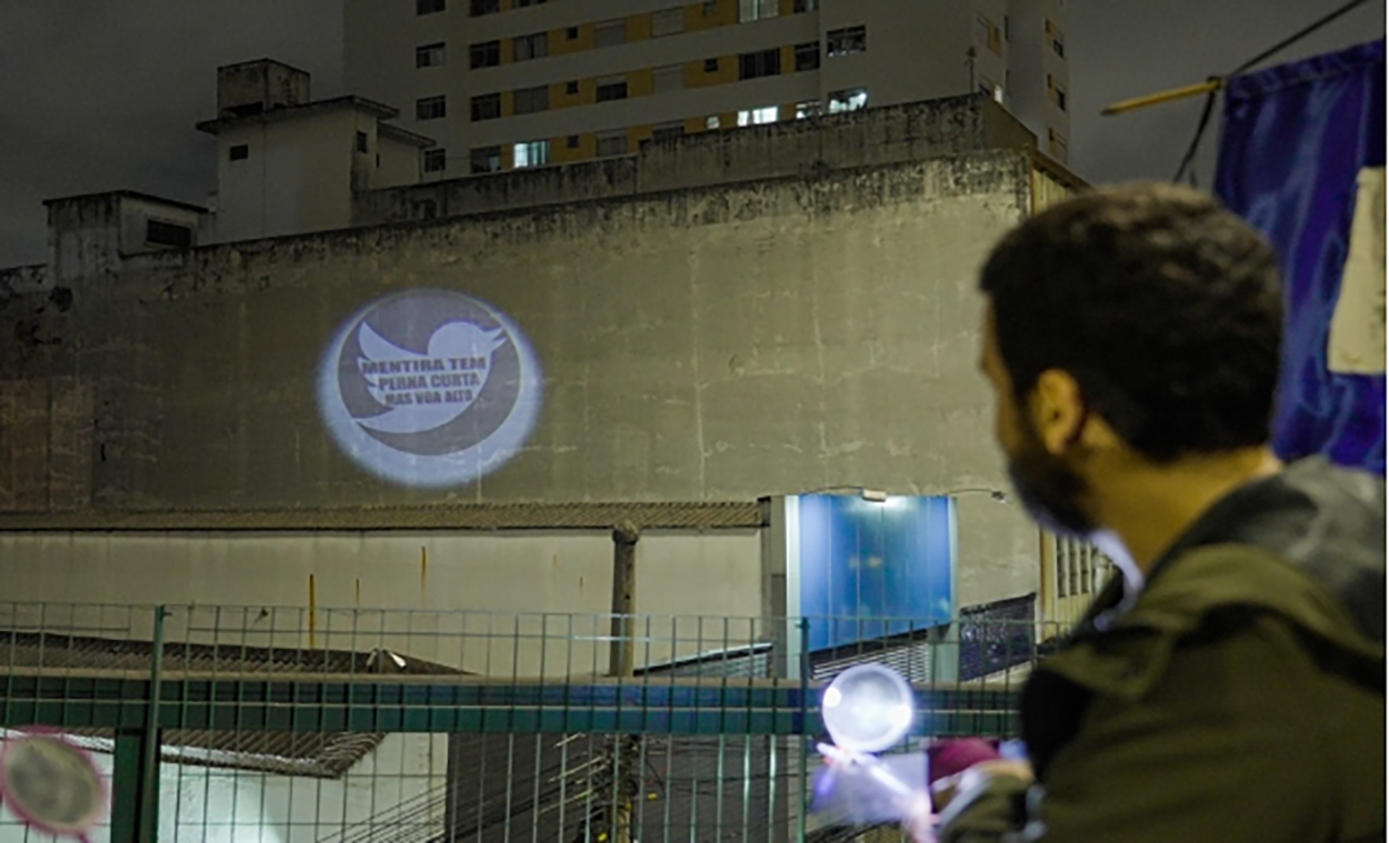 Brazilian artivist Cauê Maia using his “Bazooka Poetica” to project the poem: “Mentira tem perna curta mas voa alto” [The lie has short legs but knows how to fly high].