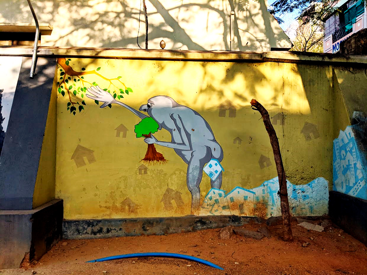 A mural showing a giant grey creature gorging on trees and the countryside and consequently excreting the built environment of the city.