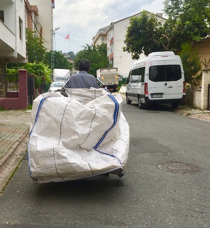 Seen from behind, a male waste picker pulls a plastic pull-cart down the street in an urban neighborhood in Istanbul, Turkey.