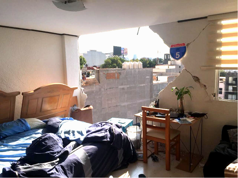 A destroyed bedroom, where a half of the bedroom wall has given way, and the city beyond is visible through the hole in the wall. The bedroom itself is in disarray, and the bedframe appears to have collapsed.