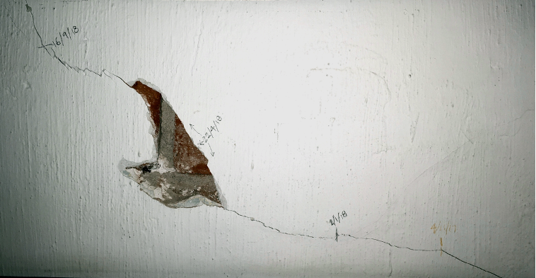 Cracks in the concrete wall that have dates scrawled alongside them.