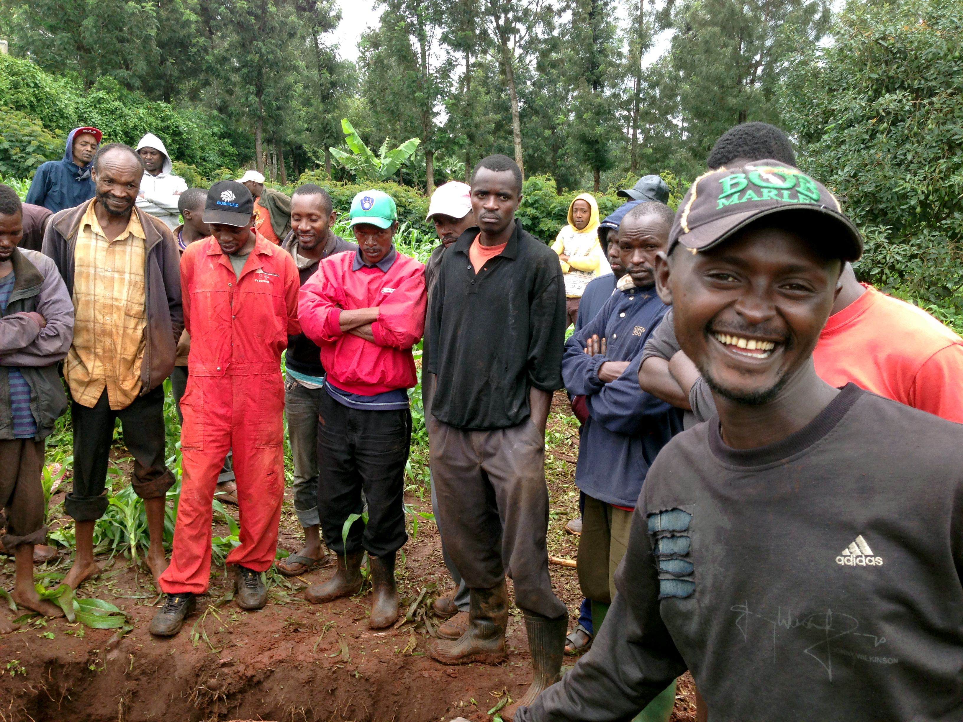 A group of men standing above a grave, out of shot to the lower left.
