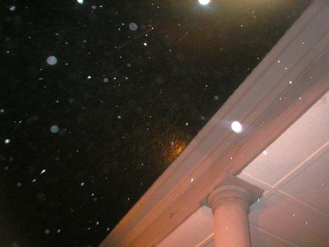 Night sky filled with visible dust illuminated by artificial light above the corner of a columned building.
