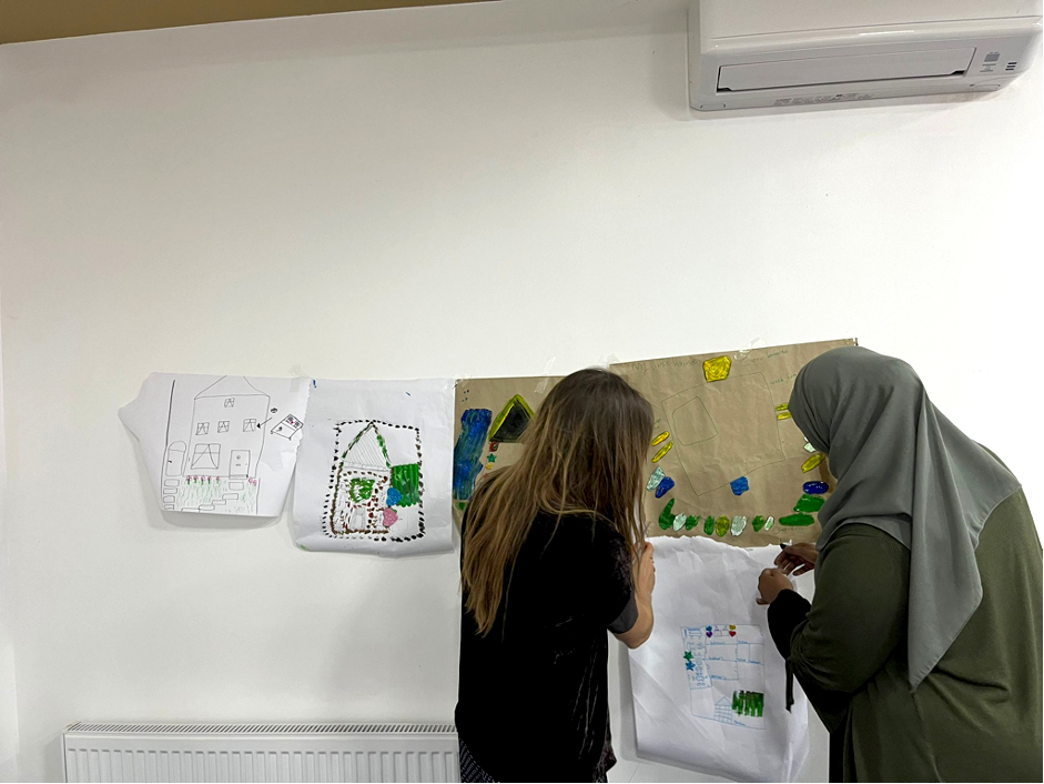 Two women pin up a piece of art to a wall.