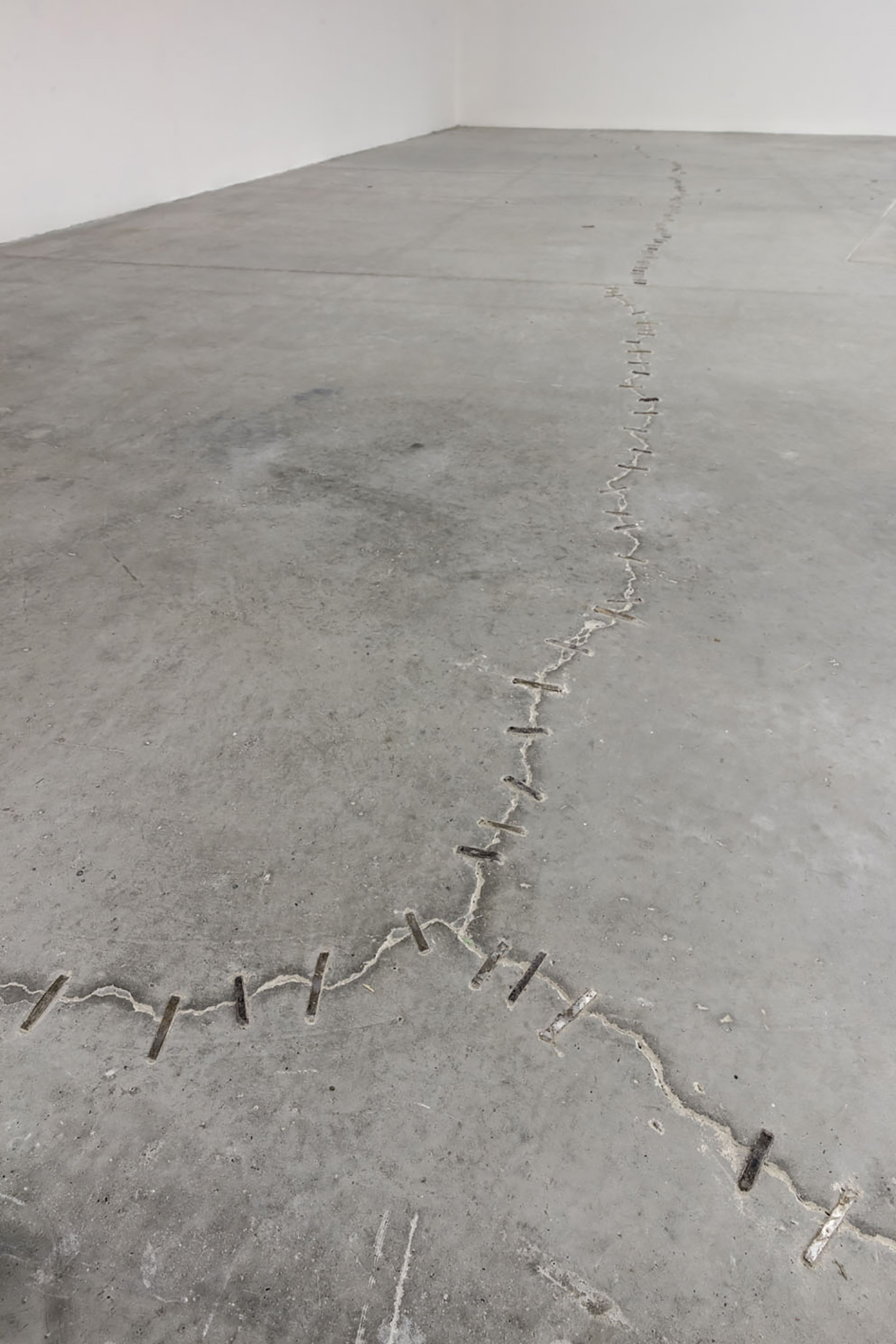 Cracked concrete floor stitched together with metal staples along a jagged fracture line.