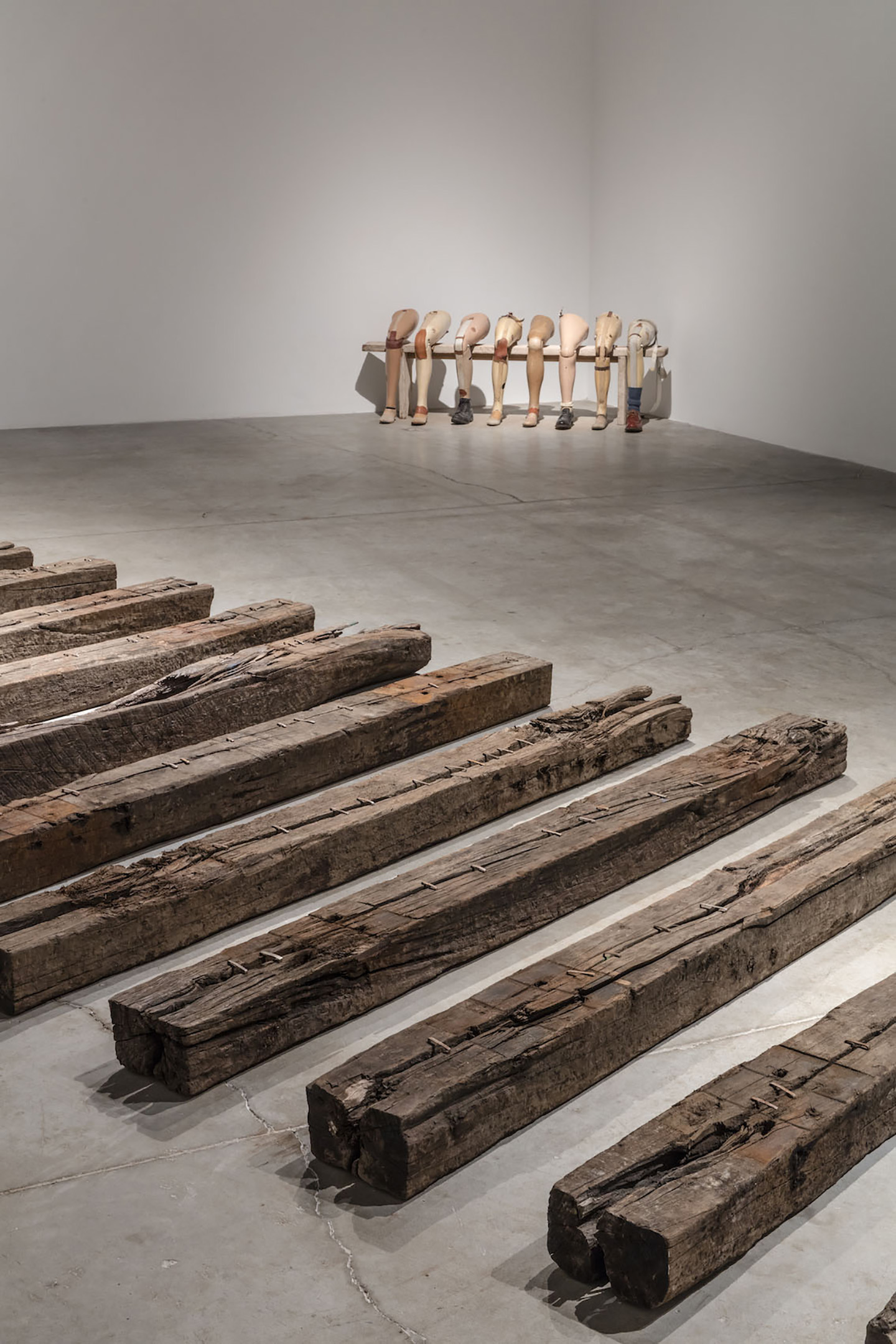 Installation of worn wooden railway sleepers laid in rows on the gallery floor, with prosthetic legs lined up against the far wall.