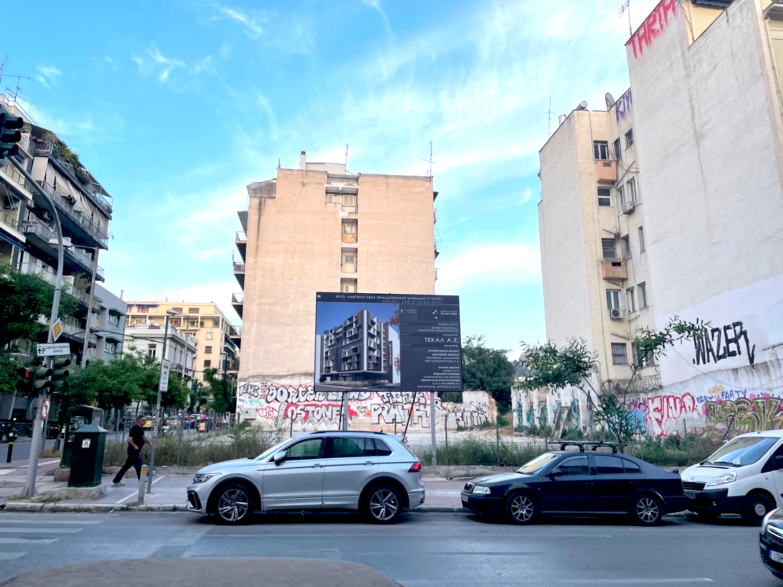 Building development advertisement on an empty fenced lot along a busy street.