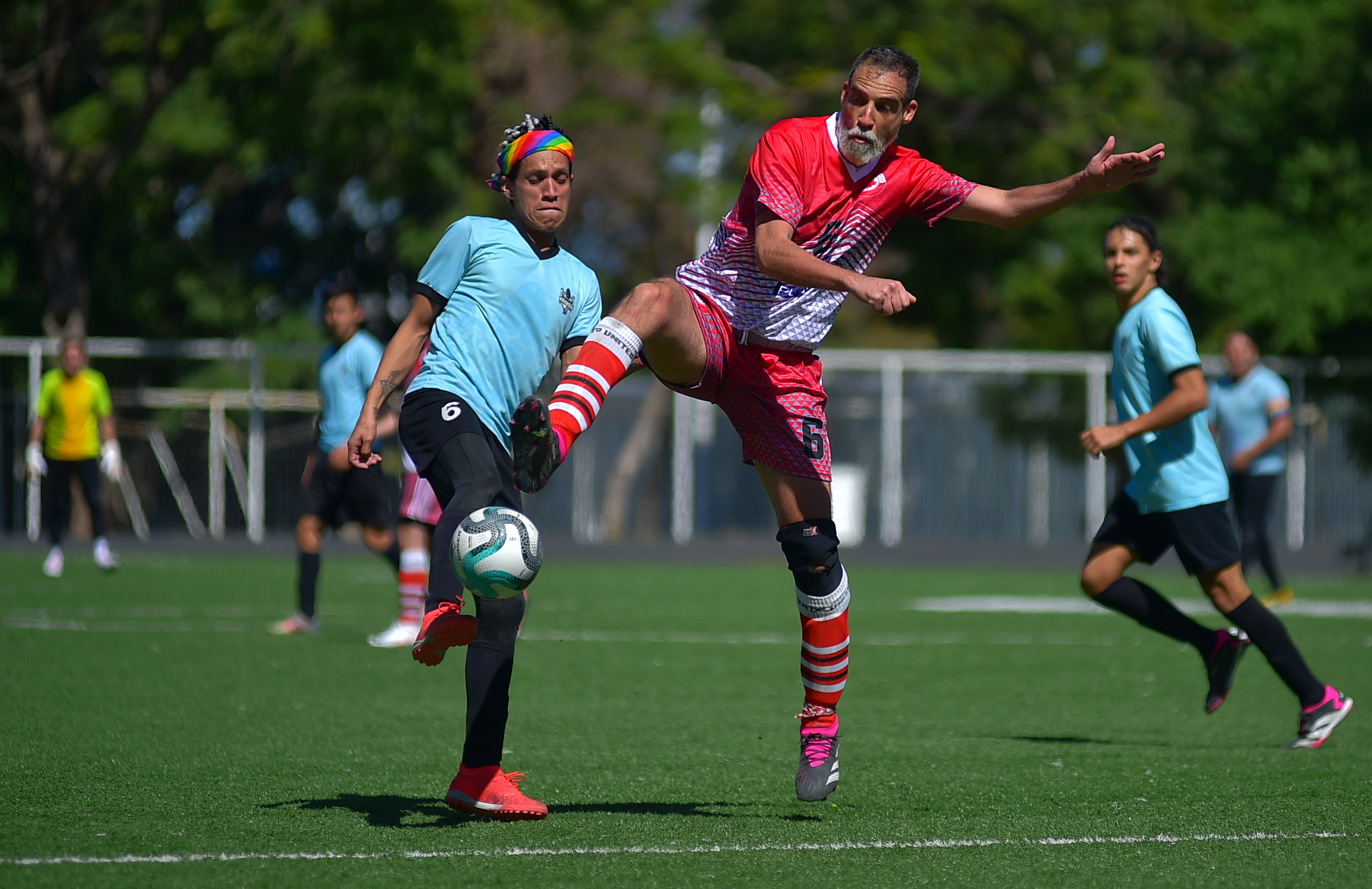 Football players of opposite teams clash feet contesting the ball, wearing blue and red jerseys respectively.