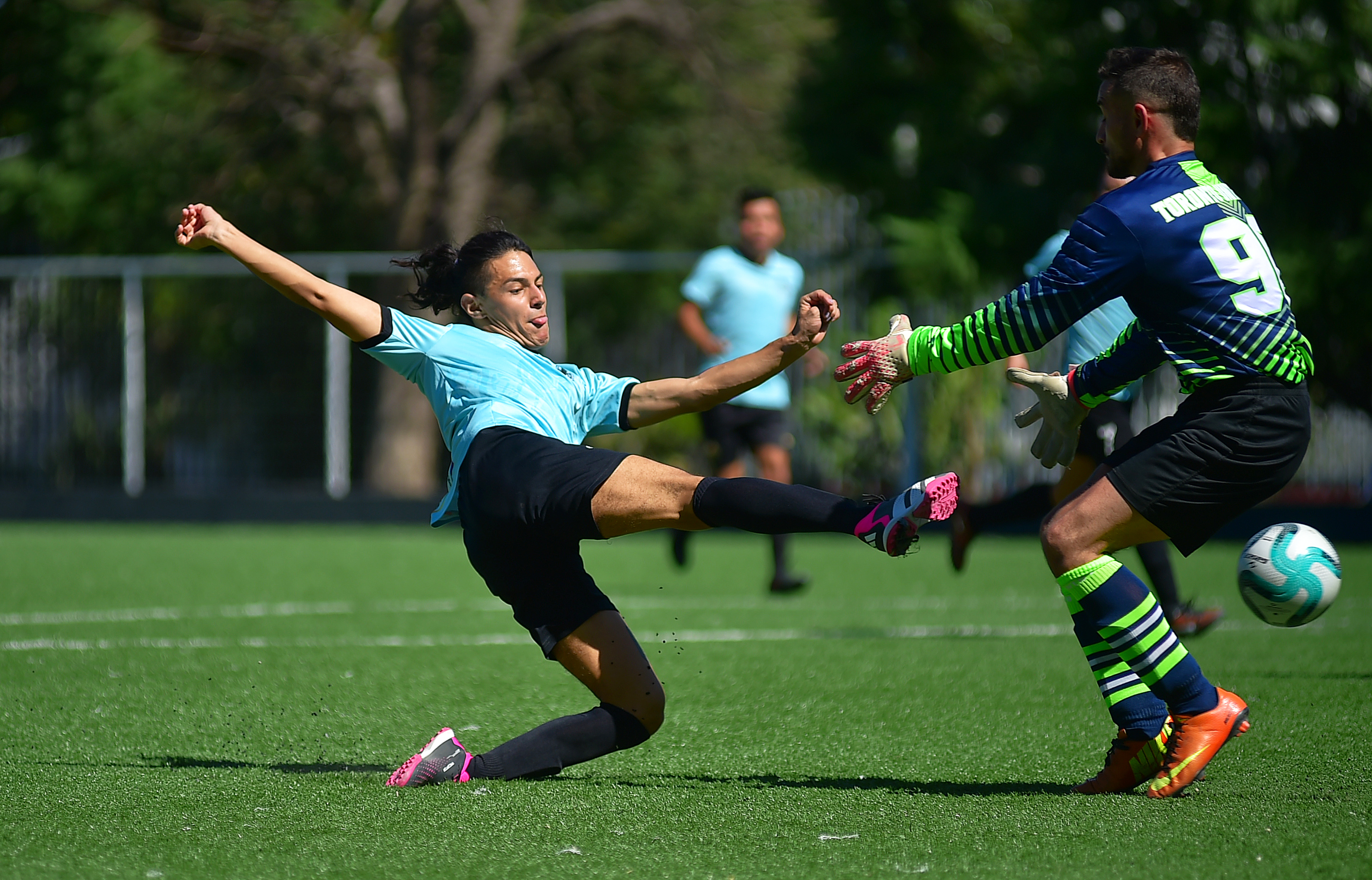 Football player stretches leg in front of opponent goalkeeper to push the ball into the net.