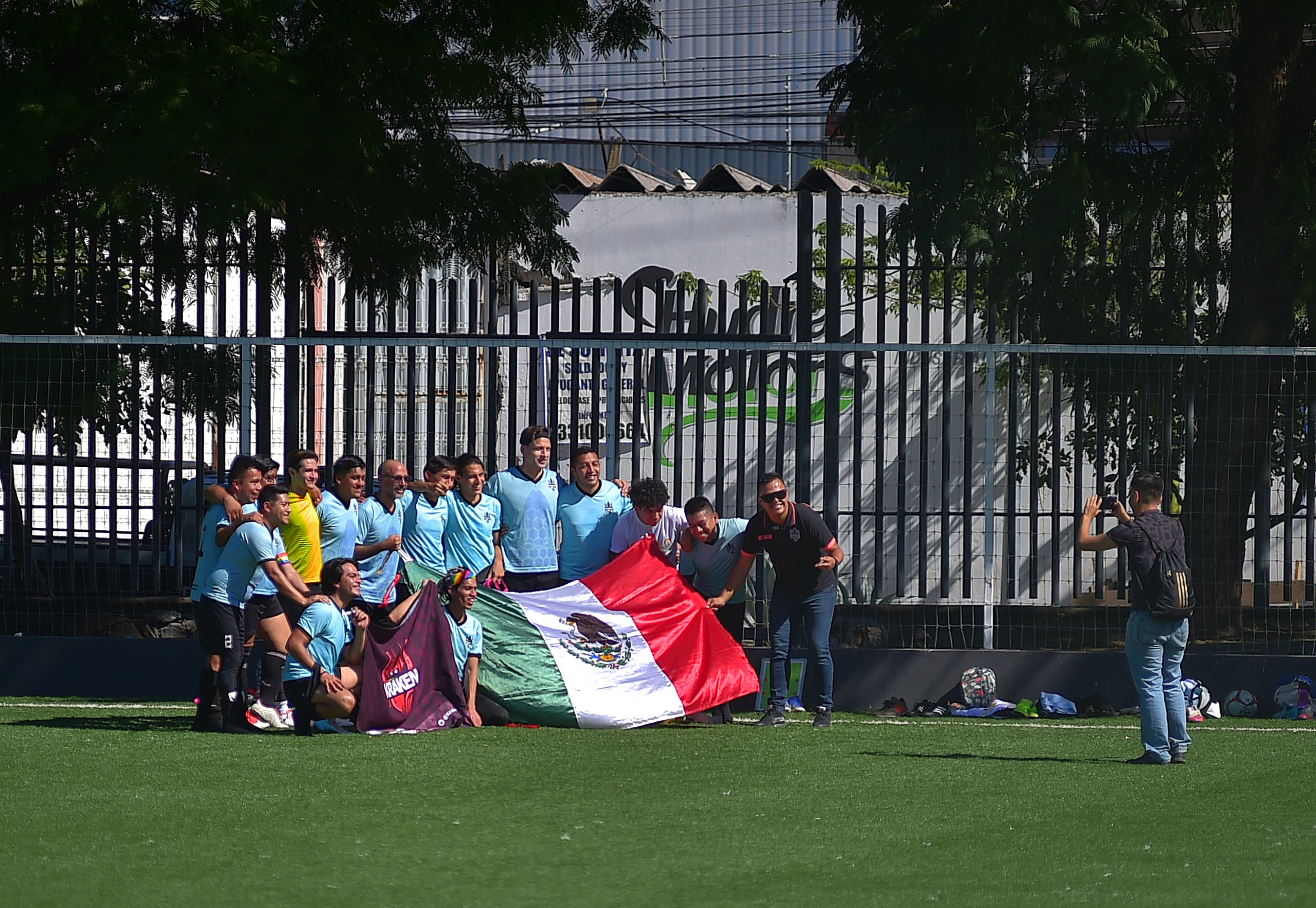 Football team poses with their team flag and the Mexican flag in a football field.